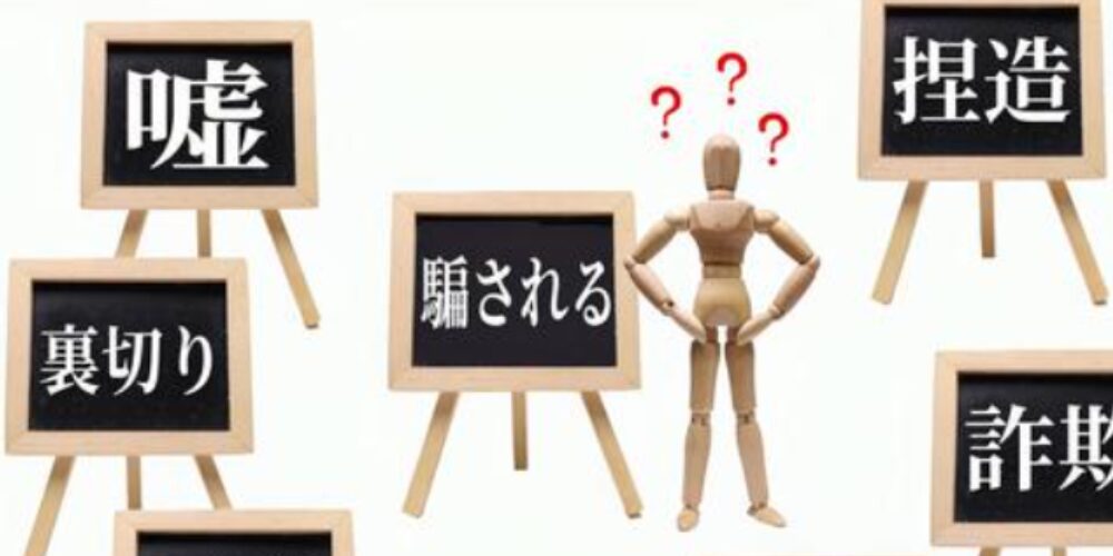 中央に疑問符が浮かぶ木製人形、周囲に「嘘」「裏切り」「騙される」「捏造」「詐欺」などの言葉が黒板に書かれている