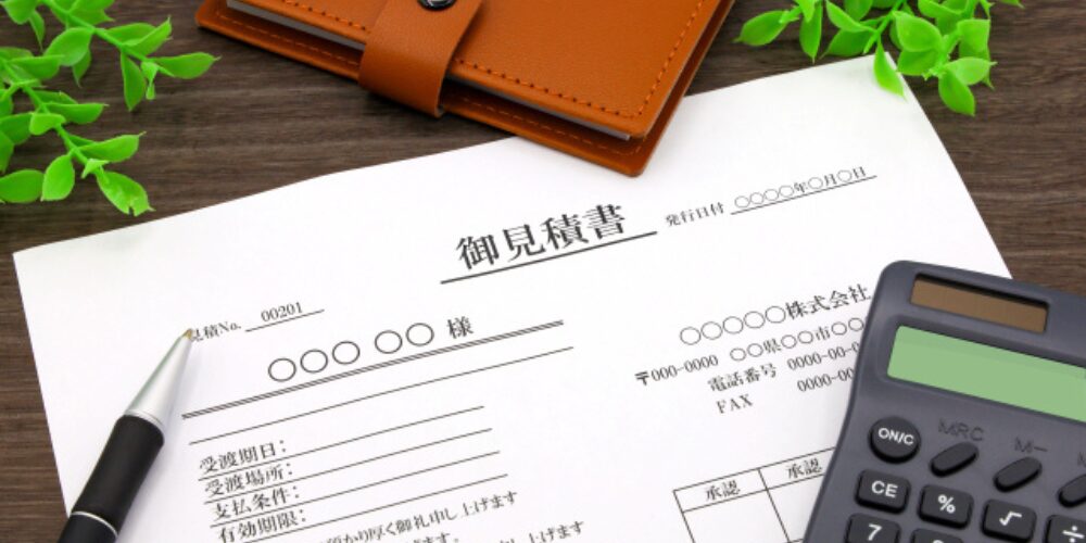 机の上に置かれた見積書と電卓、ペン、革の手帳
