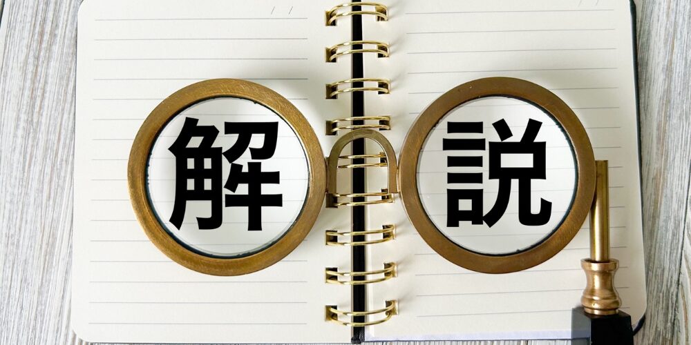 リングノートの上でメガネ形に配置した虫眼鏡に『解説』の文字が映るイメージ