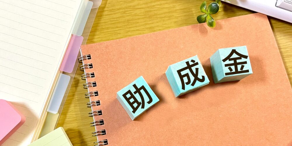 ノートの上に並ぶ青いブロックに『助成金』と書かれたイメージ写真