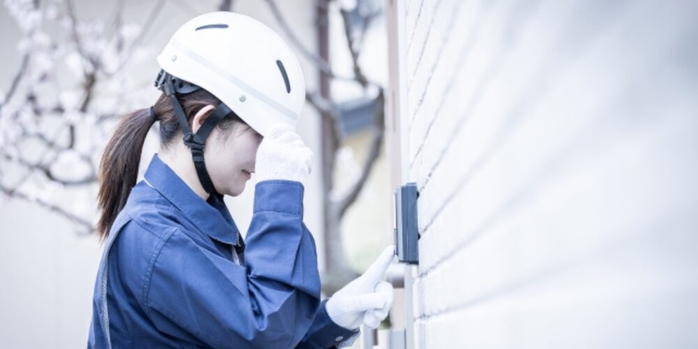 白いヘルメットを深く被り顔を隠そうとしている作業着を着た女性がインターホンを押す様子