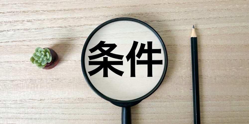 木目デスクで虫眼鏡を通して『条件』の文字を拡大した写真