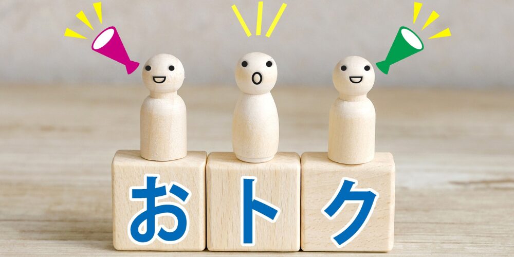 『おトク』の文字ブロックの上でメガホンを掲げる木製ピン人形のイラスト風写真