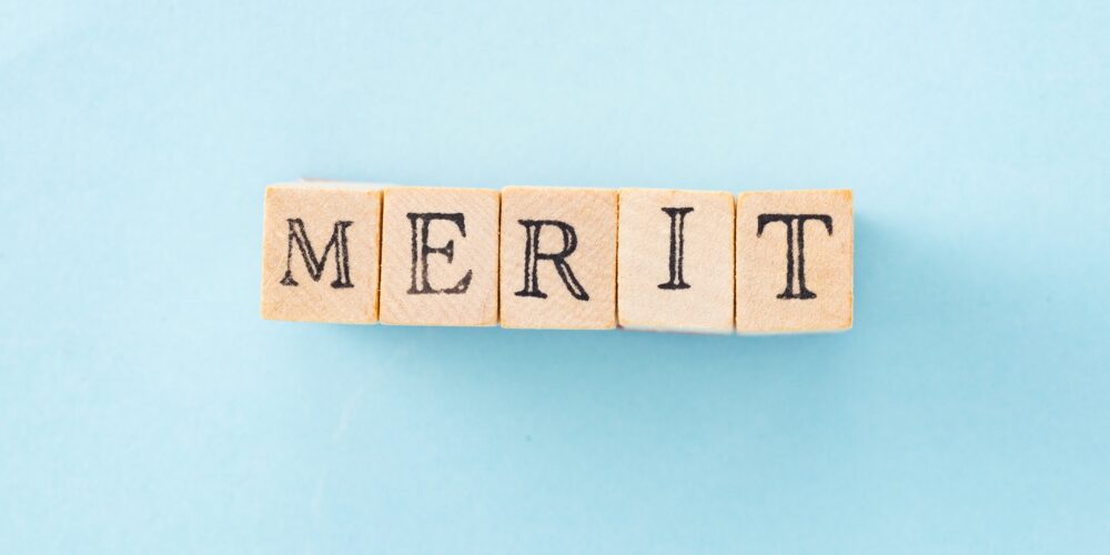 水色の背景に並べられた木製アルファベットブロックで構成された『MERIT』の文字