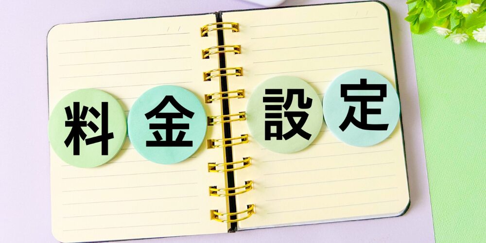 リングノートの上に並べたパステルカラーの丸いカードに『料金設定』の文字が書かれている料金プランのイメージ