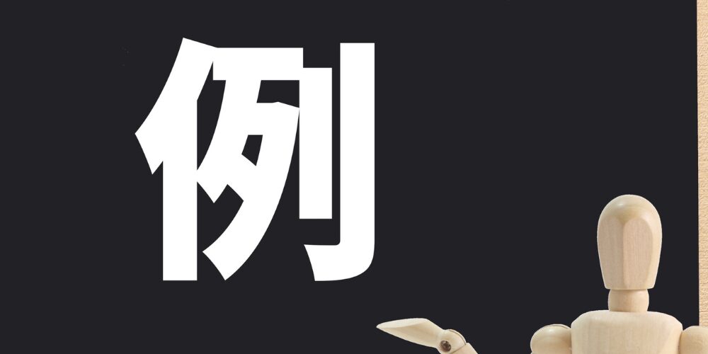 黒板に大きく描かれた『例』の文字を指差す木製マネキンのイメージ