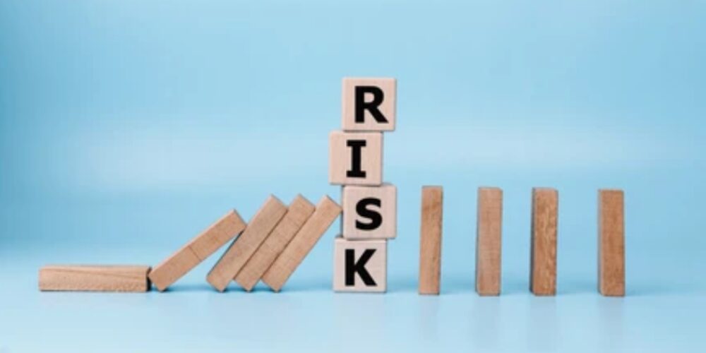 青背景の中でドミノ倒しにより「RISK」の文字が崩れ始めている様子