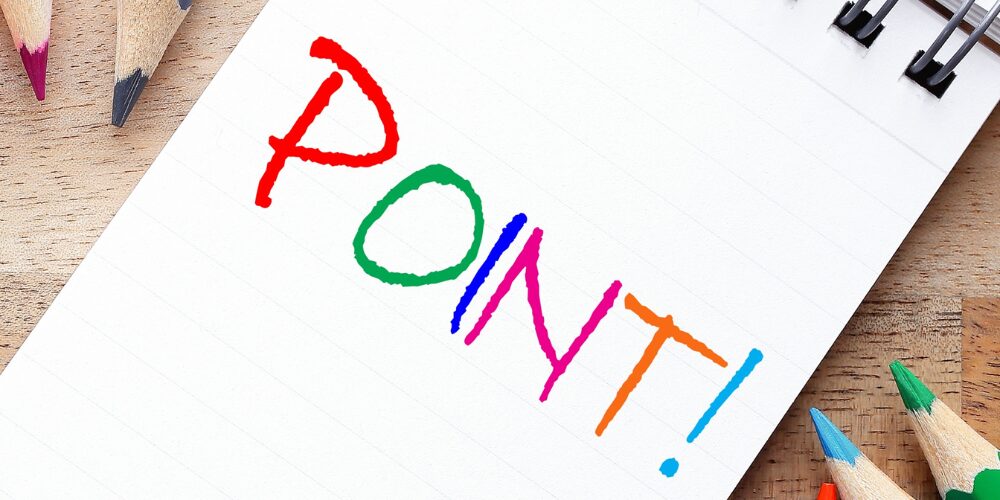 ノートに色鉛筆でカラフルに描かれた『POINT!』の文字と鉛筆のクローズアップ