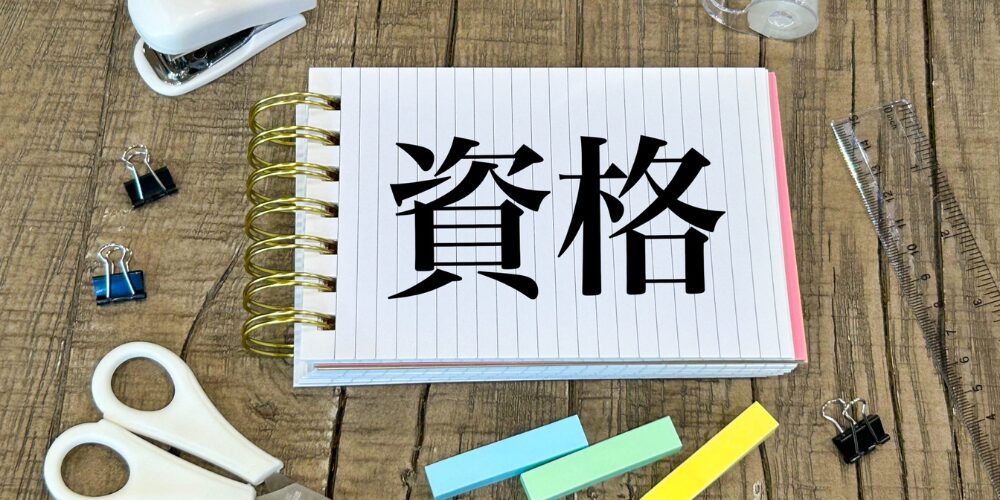 デスクに置いたリングノートに『資格』の文字、周囲に定規や文房具が並ぶイメージ