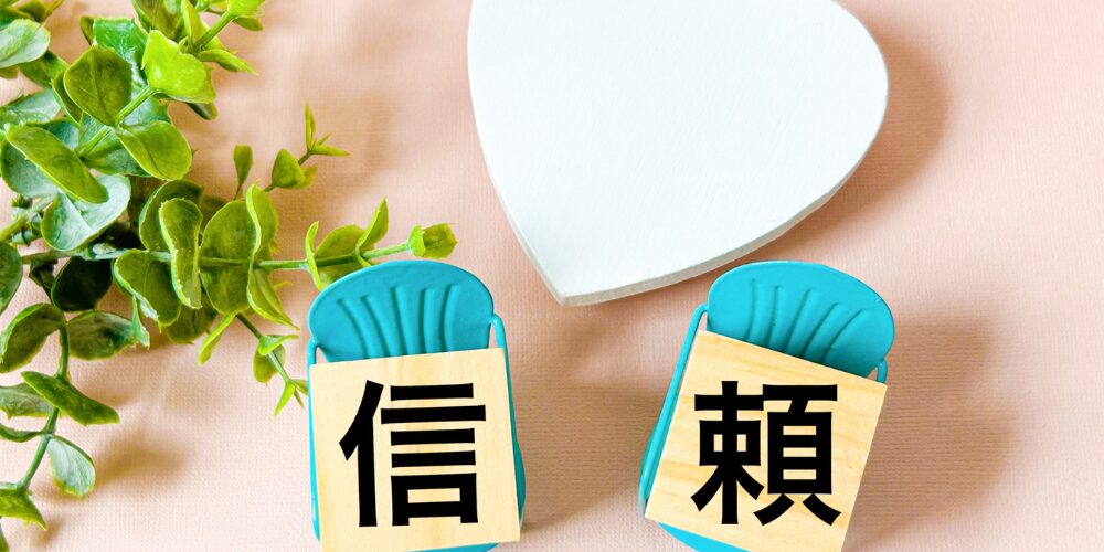 ハート型オブジェとミニチュアチェアに『信』『頼』の文字ブロックを載せ、観葉植物を添えて信頼感を演出したイメージ