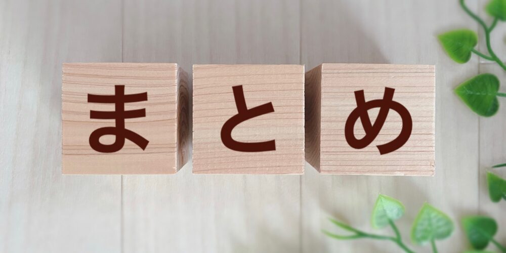 木製キューブが3つ並び、それぞれに「ま」「と」「め」の文字が刻まれ、背景には淡いグリーンの観葉植物が添えられている。