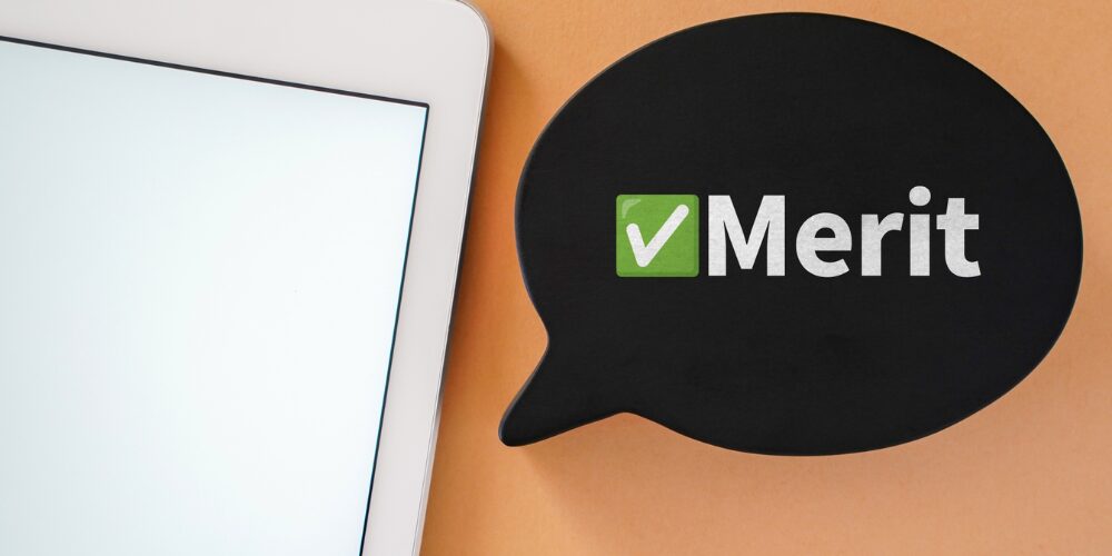 タブレットの画面端と、黒い吹き出しに緑色のチェックマークと「Merit」という文字が書かれた写真。