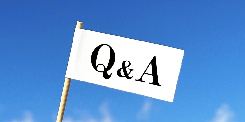 青空を背景に白い小さな旗に黒字で「Q&A」と書かれた看板を棒で掲げたイメージ。