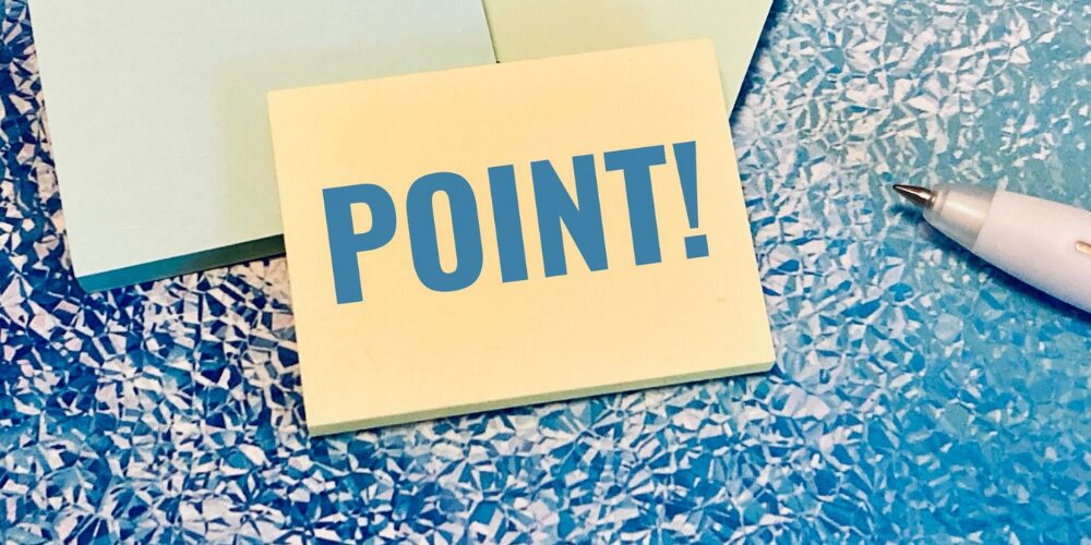 青いテーブルの上に付箋が散らばり、中心に黄色の付箋に大きく青字で「POINT!」と書かれたメモとペン。