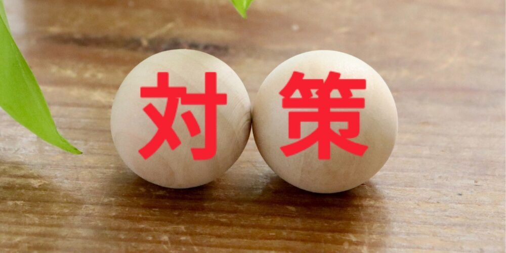 丸い木製の玉2つに赤い文字で「対」と「策」と書かれ、緑の葉が背景に添えられた写真。