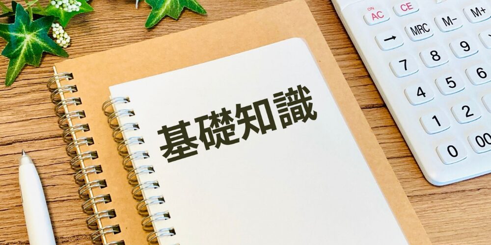 ノートに黒文字で「基礎知識」と見出しが書かれ、隣にペンと電卓が並ぶ学習イメージの机上風景。