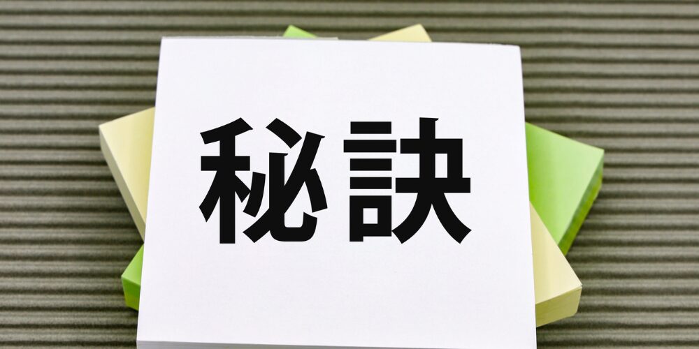 緑の葉に囲まれたメモパッドに「秘訣」と大きく書かれた積み重なった付箋の写真。