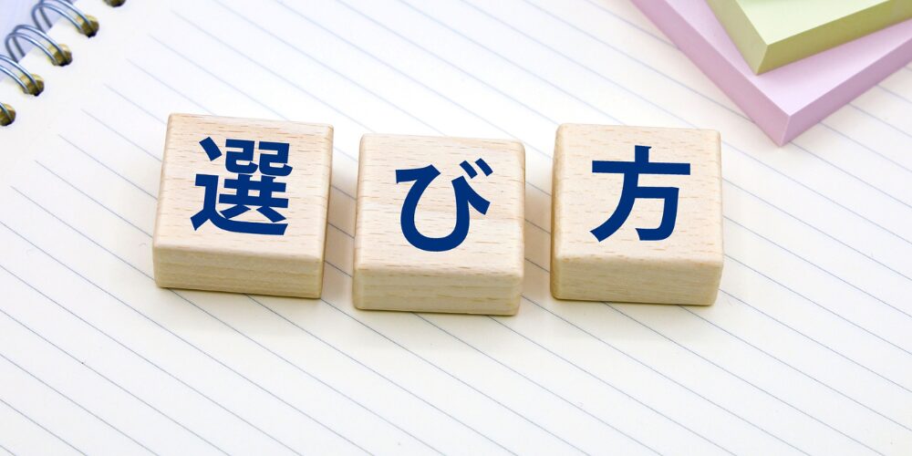 白いノートの上に木製ブロックで青い文字の「選び方」と並べられ、背後に付箋が積まれている