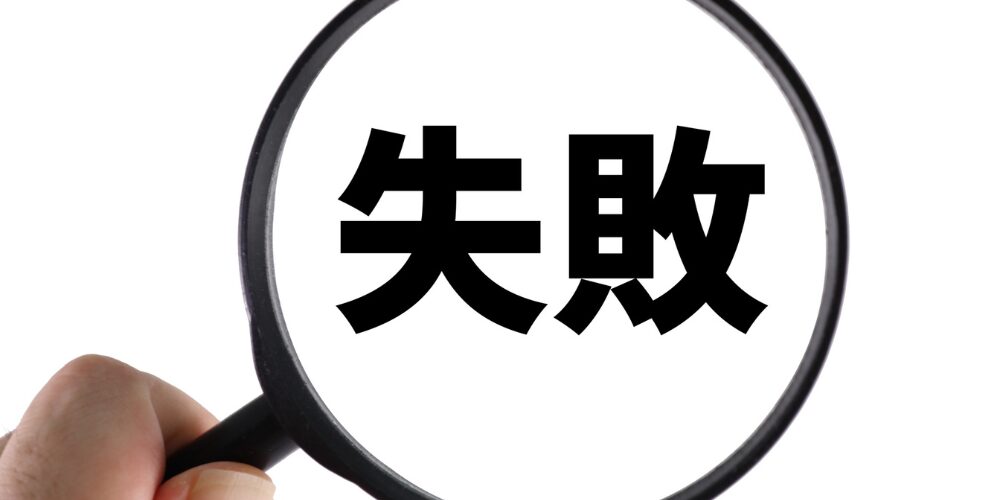手に持った虫眼鏡で黒い文字の「失敗」を拡大して映している写真